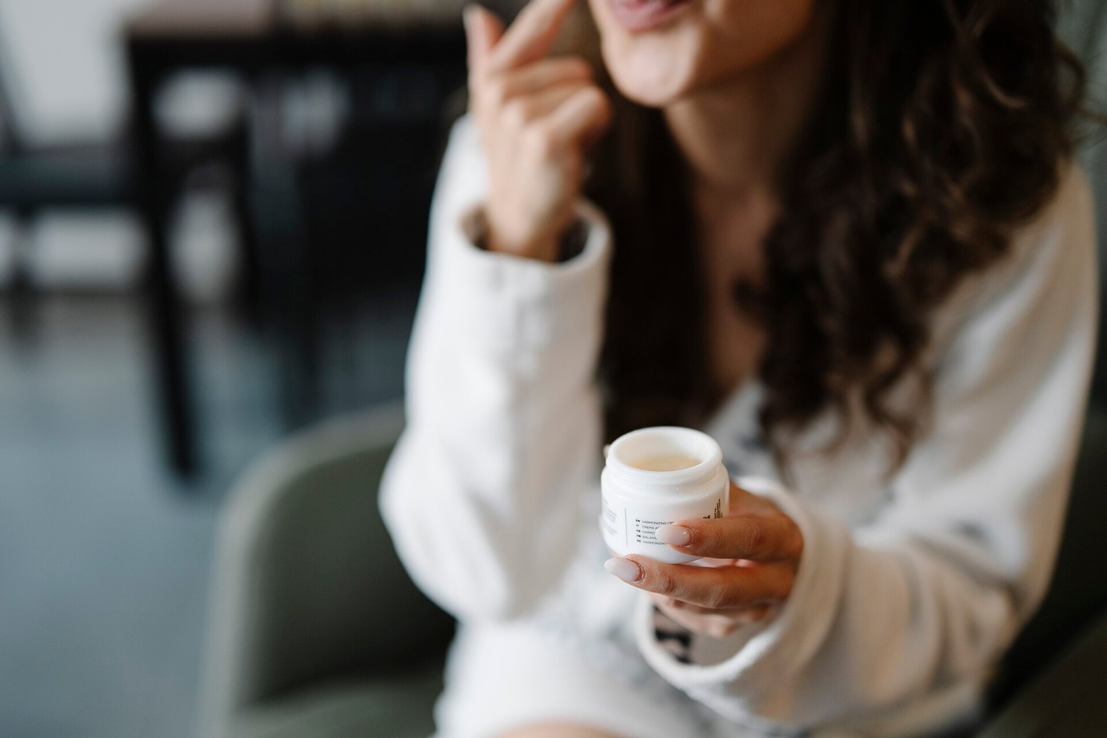 A woman applying face cream to her cheek in soft natural light
